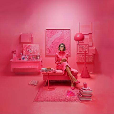 Een interieurdesigner zit op een bank in een roze kamer, gevuld met stijlvolle roze meubels.